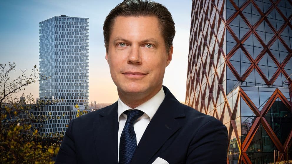 En man i kostym framför två skyskrapor i glas